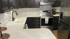 A modern kitchen with dark cabinetry, a stainless steel refrigerator, a built-in oven, and a large island with a sink and countertop.