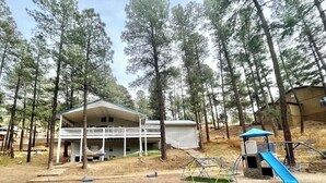 A cabin with a porch and a play area, surrounded by tall pine trees.