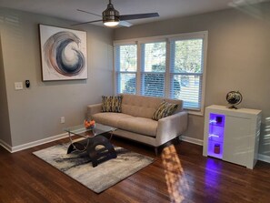 A living room with a sofa, a glass coffee table, a rug, a ceiling fan, and a side table with a globe. - Outdoor Kitchen+Free Arcade+5 Miles to Downtown (Atlanta)