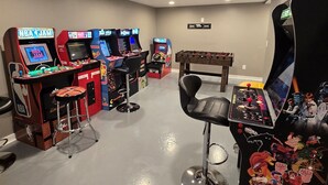 A room with multiple arcade machines, a foosball table, and a bar area with stools. - Outdoor Kitchen+Free Arcade+5 Miles to Downtown (Atlanta)