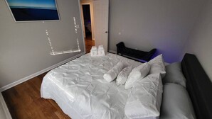 A bedroom with a large bed, a wall-mounted TV, and a door leading to another room. - Outdoor Kitchen+Free Arcade+5 Miles to Downtown (Atlanta)