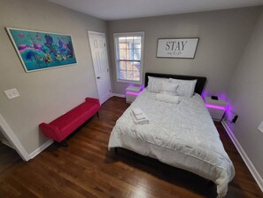 A bedroom with a large bed, a red bench, a window with blinds, and a wall with a 'STAY' sign. - Outdoor Kitchen+Free Arcade+5 Miles to Downtown (Atlanta)