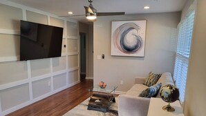 A modern living room with a flat-screen TV mounted on the wall, a glass coffee table, a grey sofa with decorative pillows, and a globe on a side table. - Outdoor Kitchen+Free Arcade+5 Miles to Downtown (Atlanta)