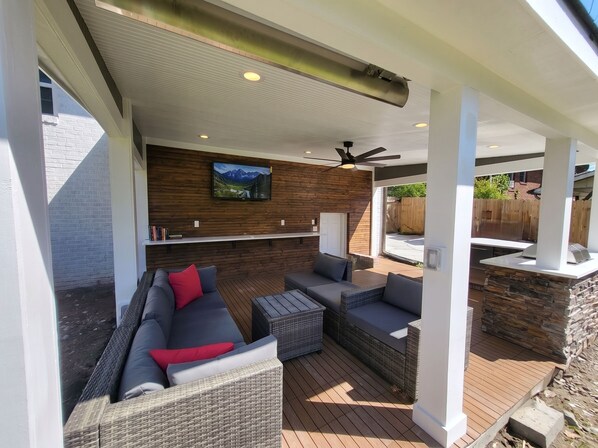 An outdoor patio with a sofa, chairs, and a television mounted on a wooden wall.