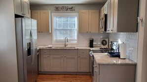 A kitchen with wooden flooring, a stainless steel refrigerator, and beige cabinets. - Outdoor Kitchen+Free Arcade+5 Miles to Downtown (Atlanta)