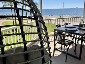 A balcony with a view of the ocean, a table with chairs, and a hanging chair. - APARTBEACH BELL RACO BEACH FRONT (La Pineda)