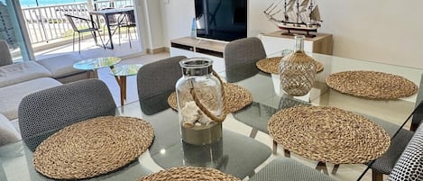 A modern living room with a glass table, woven poufs, a ship model, and a TV.