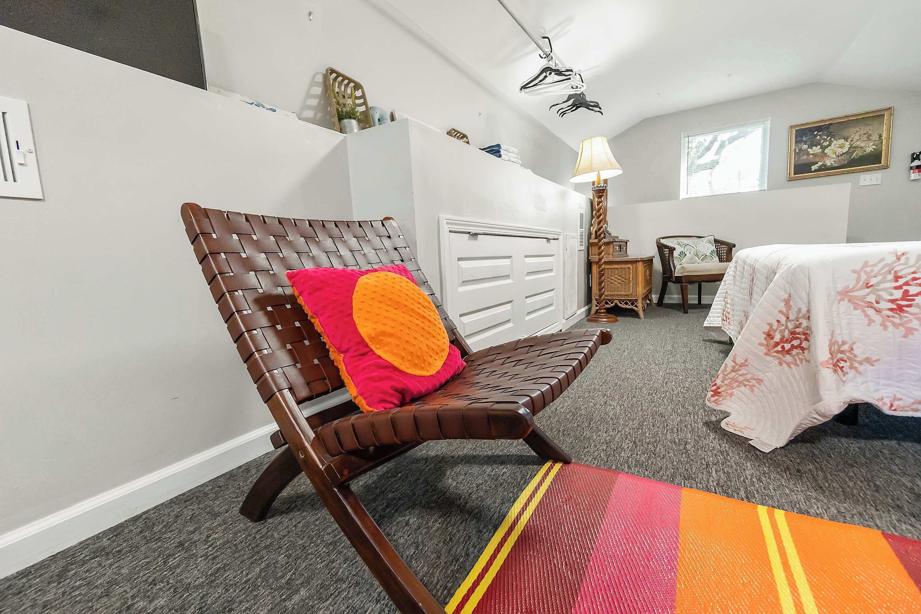 A room with a wooden chair, a bed with a floral bedspread, a lamp, a chair, and a radiator.