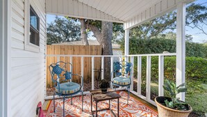 A covered porch with two blue chairs, a small table, and a potted plant.