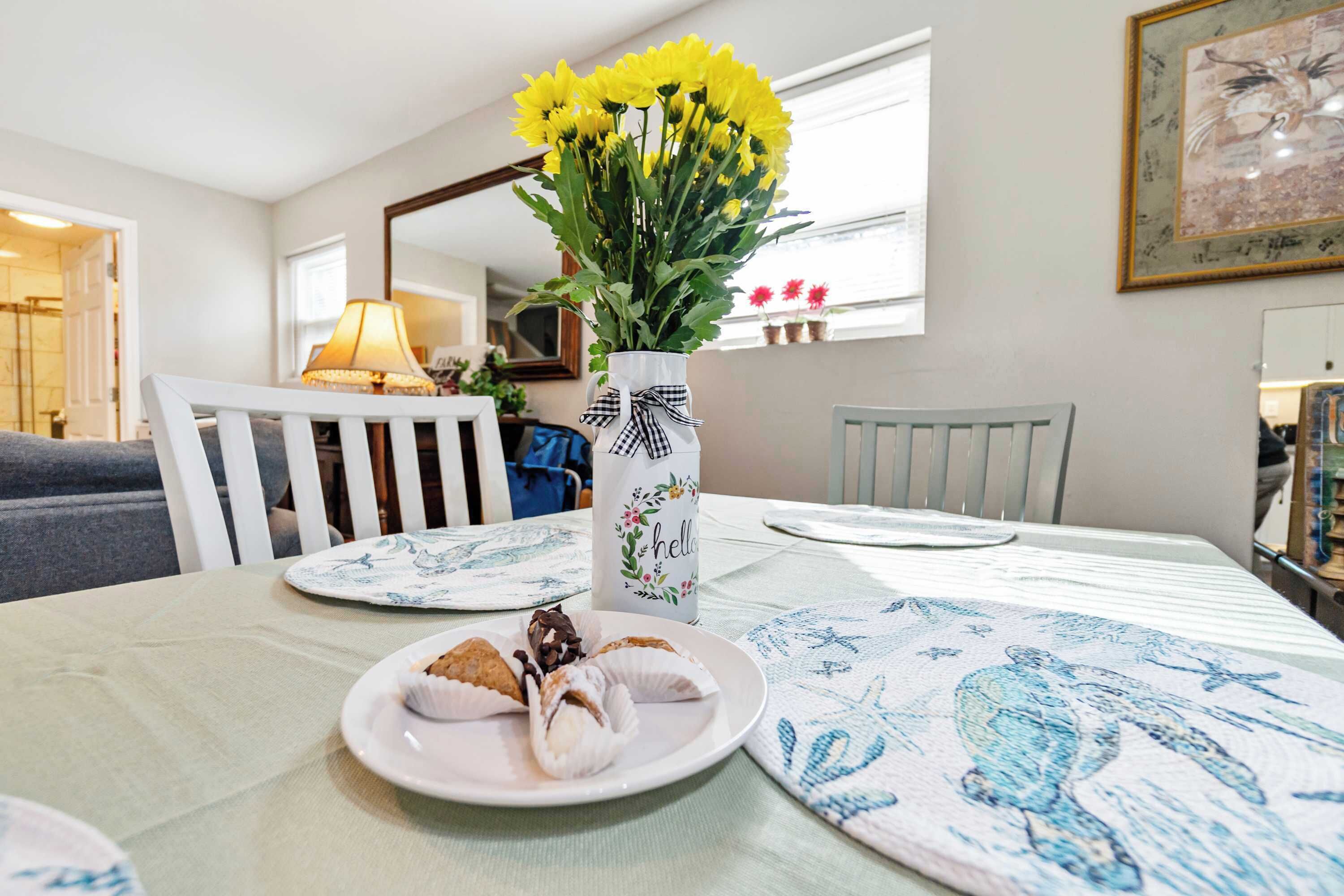 Une table à manger ornée d’un vase de fleurs jaunes, d’une assiette de pâtisseries et d’une nappe à motifs bleus.