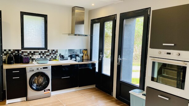 A modern kitchen with a washing machine, a built-in oven, and a large window. - Pleasant duplex, air conditioning and garden (Montmorency)