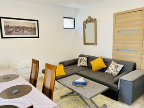 A living room with a sofa, a coffee table, a framed cityscape picture, a mirror, and a wooden wardrobe.