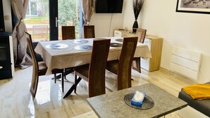 A dining area with a table set for four, a television mounted on the wall, and a framed picture above the table. - Pleasant duplex, air conditioning and garden (Montmorency)