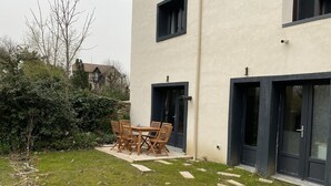 A modern building with a patio area featuring a wooden table and chairs. - Pleasant duplex, air conditioning and garden (Montmorency)