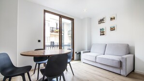 A modern living room with a round wooden table, black chairs, a grey sofa, and a balcony with a railing. - VLC HOST - Eixarchs 4 (València)