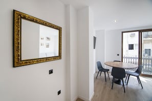 Een eethoek met een ronde tafel en stoelen, een grote spiegel met een versierde lijst, en uitzicht op een balkon door een glazen deur.