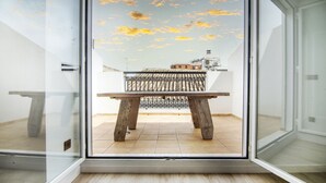 A room with a sliding glass door leading to an outdoor balcony with a wooden table and a metal railing. - VLC HOST - Eixarchs 5 (València)