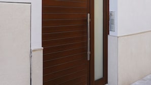 A large wooden door with a sliding glass panel, a metal handle, and a small electronic keypad on the wall beside it. - VLC HOST - Eixarchs 5 (València)