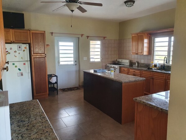 A kitchen with wooden cabinets, a refrigerator, a stove, and a ceiling fan.