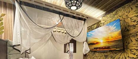 A bedroom with a bed, a TV, a coffee table, and a wall with a floral pattern.