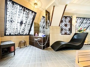 A modern spa room with a black lounge chair, a small stool, and a vanity with a mirror.