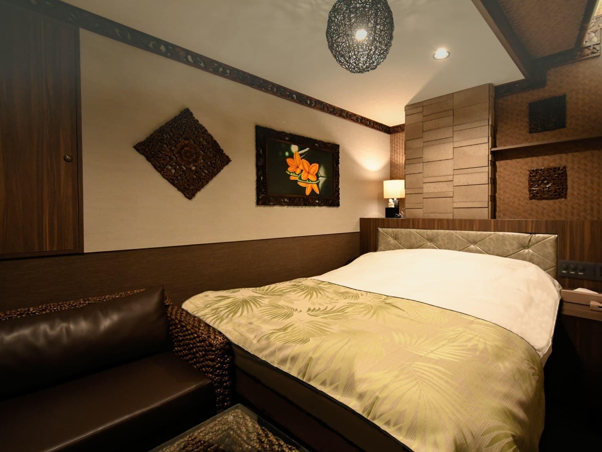 Una habitación de hotel con cama, mesita de noche, lámpara, un adorno de pared e iluminación en el techo.