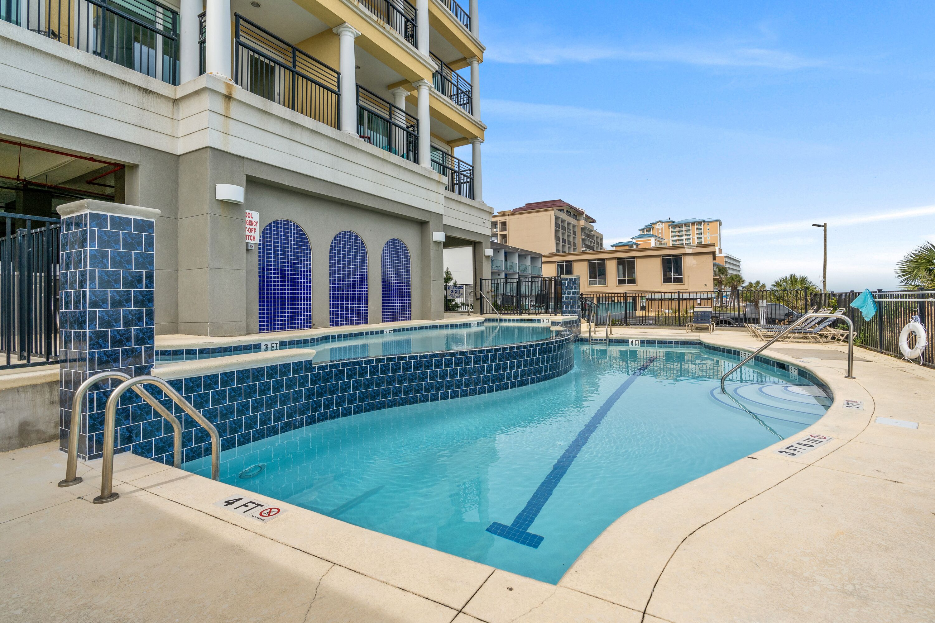 A swimming pool with a tiled edge, a lifeguard tower, and a building with balconies in the background.
