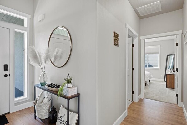 A hallway with a white door, a mirror, a console table with decorative items, and a sign on the wall.