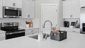 Een moderne keuken met witte kasten, roestvrijstalen apparatuur en een centraal eiland met een mand vol tijdschriften.