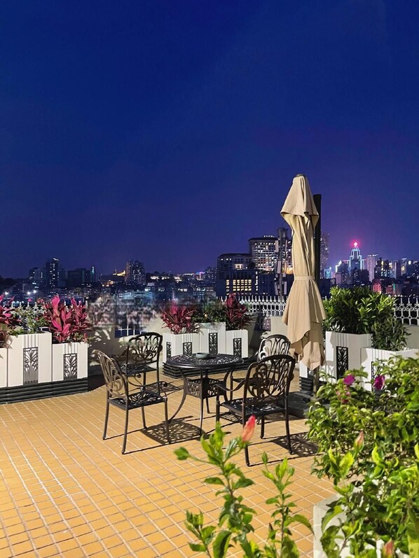 A rooftop terrace with outdoor seating and a city skyline view at night.