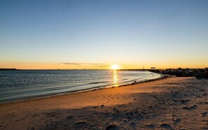 Una playa al atardecer con un mar tranquilo, una orilla arenosa y un muelle que se adentra en el agua.