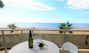 Ein Tisch mit einer Flasche und einem Glas auf einem Balkon mit Blick auf einen Strand.