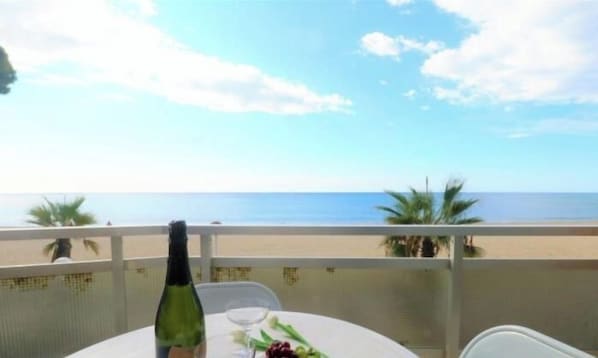 Una taula amb una ampolla i un got, un plat amb menjar, i vista a la platja i l'oceà.