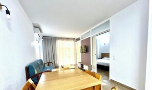 A room with a wooden dining table, blue sofa, and a bed with a wooden headboard.