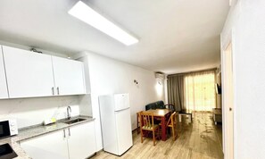 A compact kitchen with a refrigerator, microwave, and sink. There is a dining area with a table and chairs.