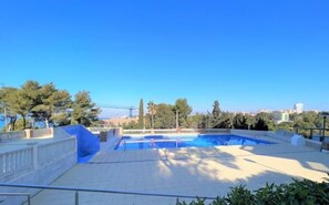 Una piscina con cielo azul despejado, árboles y edificios a lo lejos.