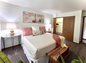 Un dormitorio ordenado con cama, mesitas de noche, una lámpara y un banco de madera.