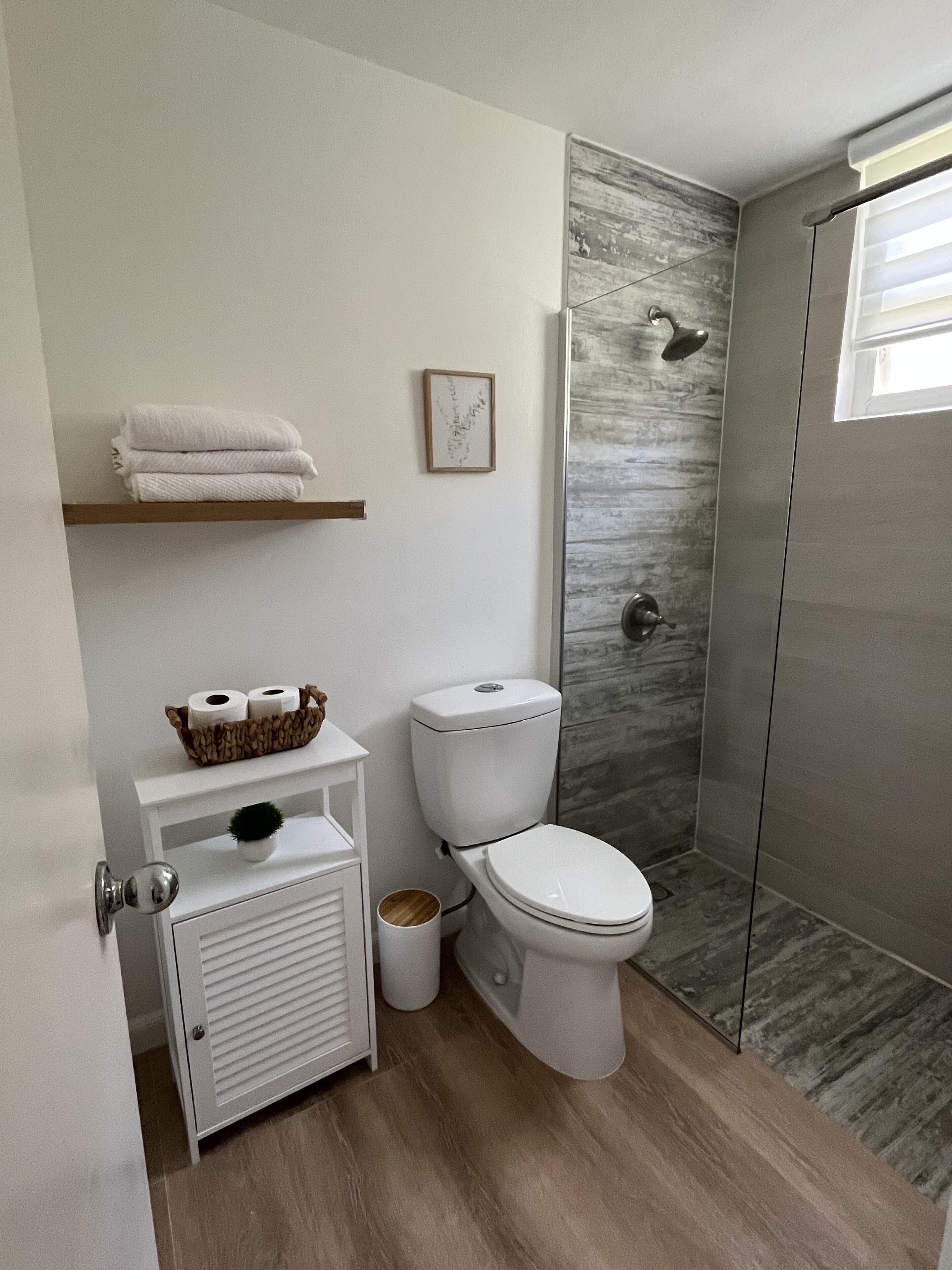 Ein modernes Badezimmer mit Toilette, Dusche und einer kleinen Ablage mit Handtüchern und Pflegeprodukten.
