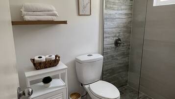 Ein modernes Badezimmer mit Toilette, Dusche und einer kleinen Ablage mit Handtüchern und Pflegeprodukten.