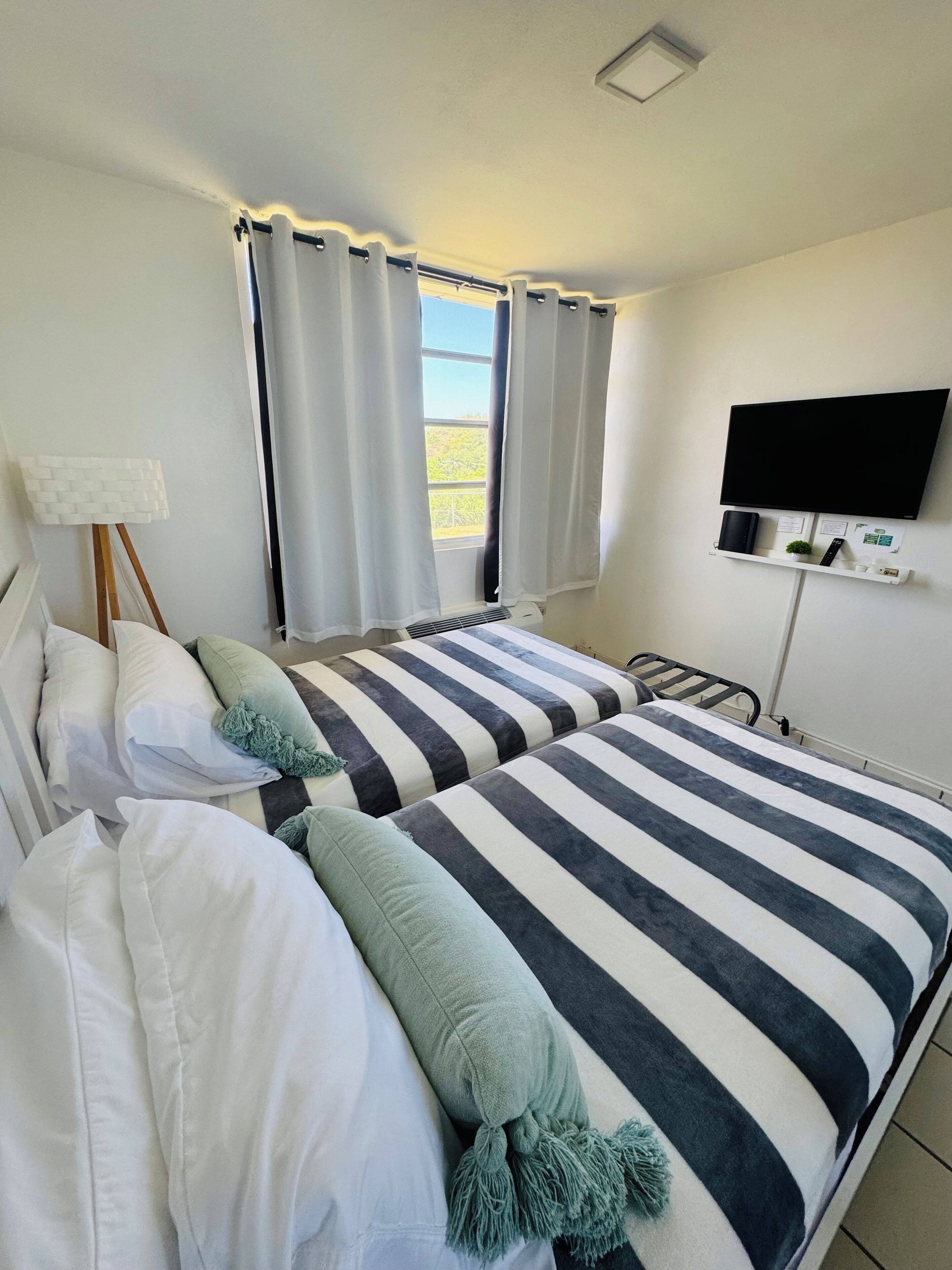 A hotel room with two beds, a TV mounted on the wall, and a window with curtains.
