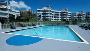 A swimming pool with a blue deck, surrounded by white buildings with balconies, under a clear sky. - Spacious 3 bedroom apartment with sea view short drive to ferry station. (Ceiba)