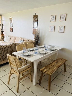 Un comedor con una mesa blanca dispuesta para cuatro personas, rodeada de sillas de mimbre y un banco.