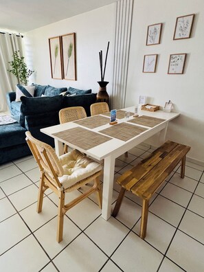 Un comedor con una mesa blanca, individuales tejidos y sillas de madera.
