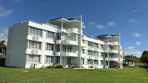 A multi-story building with balconies, a flat roof, and a grassy lawn in front. - Spacious 3 bedroom apartment with sea view short drive to ferry station. (Ceiba)