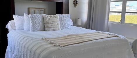Una cama grande con ropa blanca, cabecera y mesita de noche con lámpara.