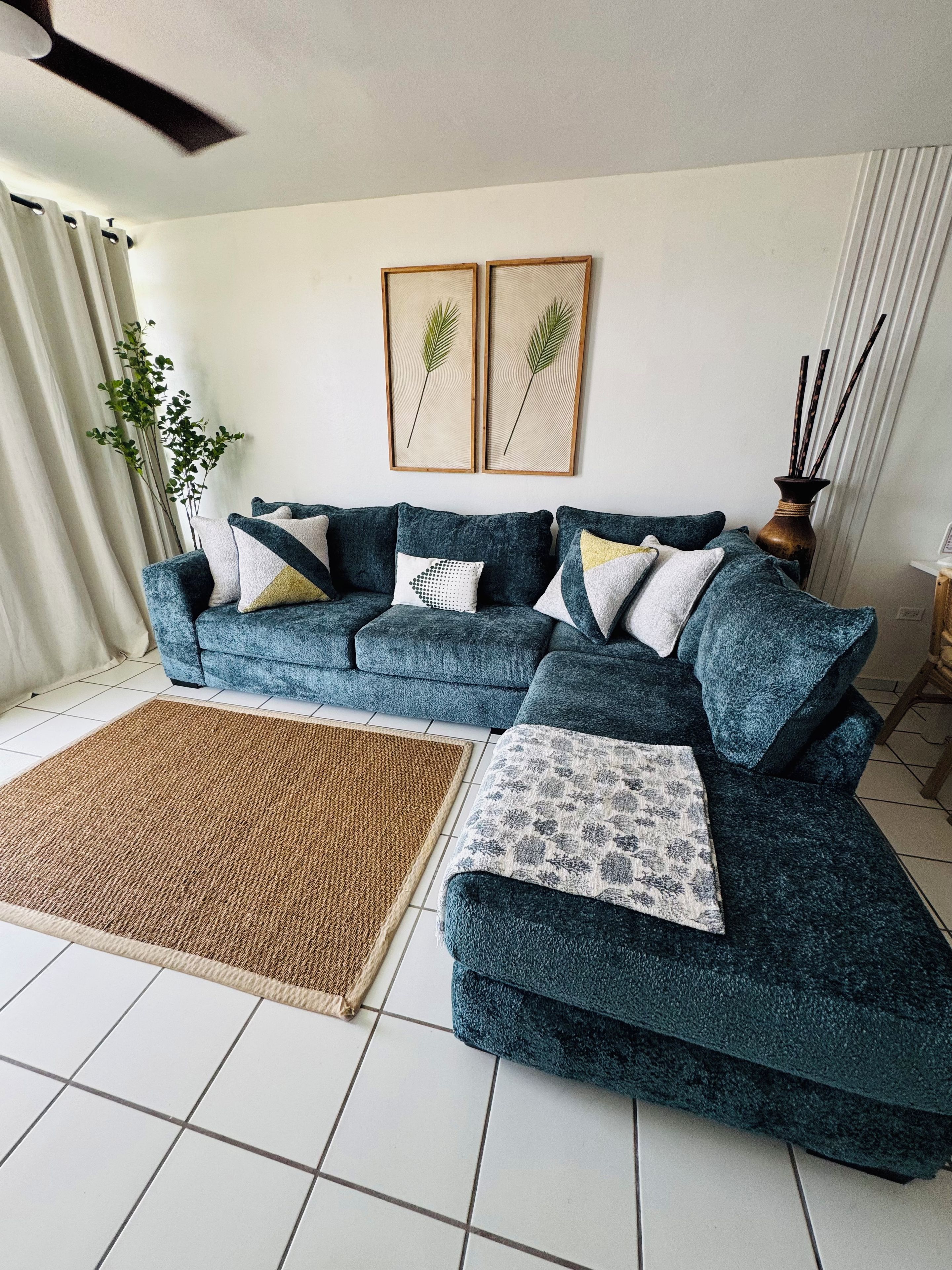 A living room with a sectional sofa, a woven rug, and two framed wall art pieces.