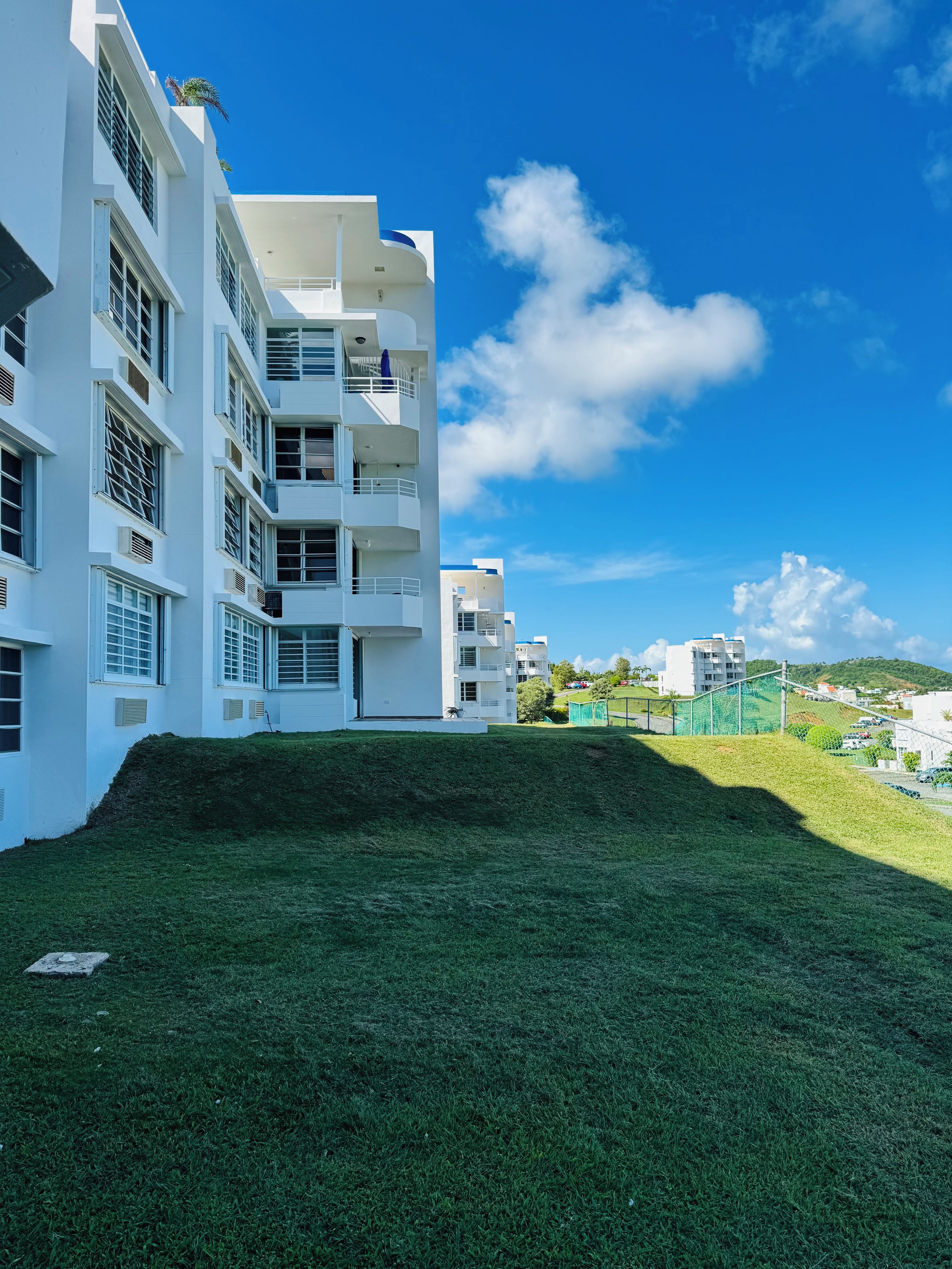 A modern building with multiple balconies and a grassy area in front.