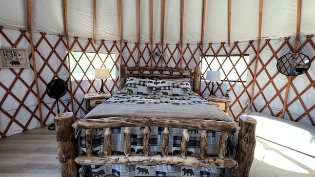 A bed with a wooden frame and a checkered blanket, a wall-mounted mirror, and a sign saying "Don't wake the bear".