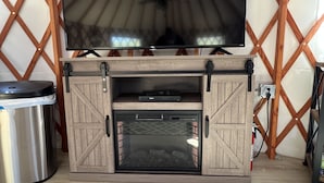 A wooden entertainment center with a flat-screen TV, a built-in grill, and a trash can.