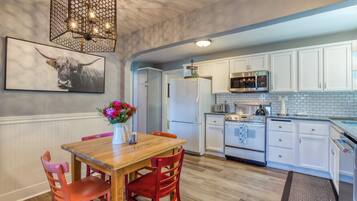 A kitchen with white cabinets, a wooden dining table with red chairs, a chandelier, and a bull-themed artwork.